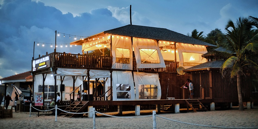 Labadi Beach scene with beach furniture, umbrellas, palm trees, people and the sea.