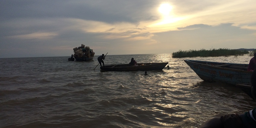 People boating at Lake Tanganyika with a cargo boat and sunset in the background