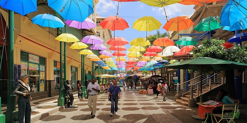 Le caudan arts and craft market with people walking under colourful hanging umbrellas.