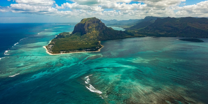 Le Morne of Mauritius, covered in green under the blue sky, is surrounded by a waterbody
