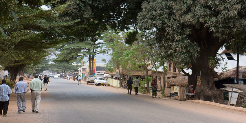 Street of Kigoma with people walking and multiple cars parked on the side of the street