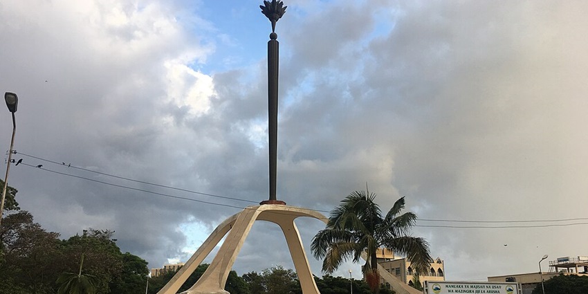 Arusha torch tower in the middle of a street in Arusha with people standing and signboards.