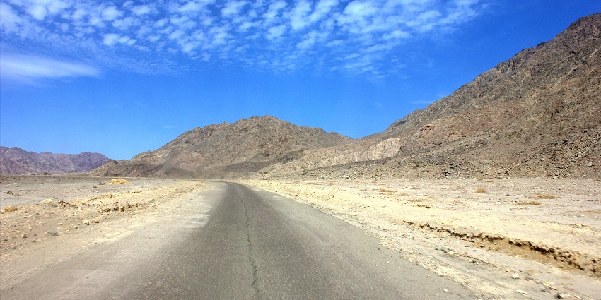 A road made of concrete is showcased, being surrounded by the majestic mountains