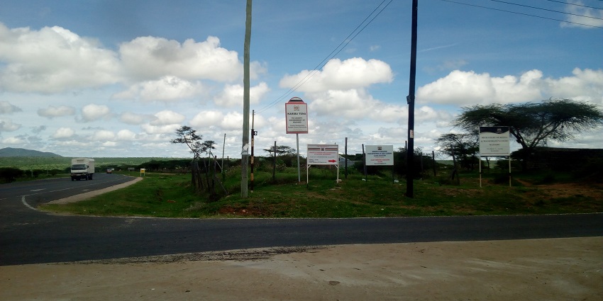 Vehicle on the road connecting Kajiado County and Namanga with boards on the side.