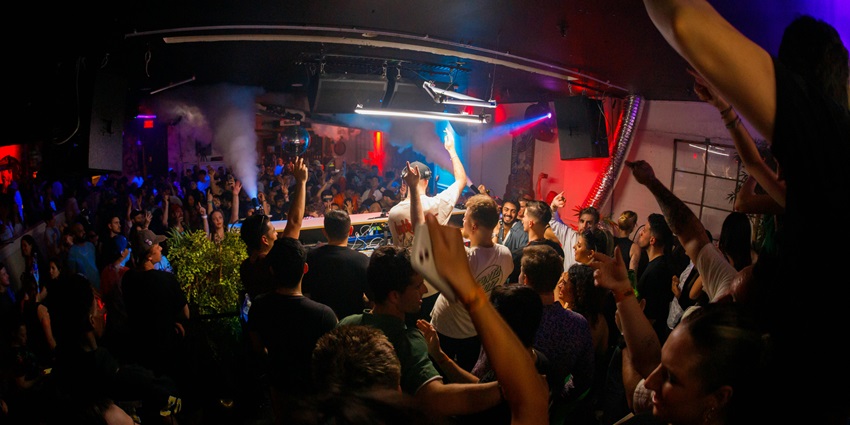 People dancing in a packed nightclub and surrounding the DJ under colourful lights