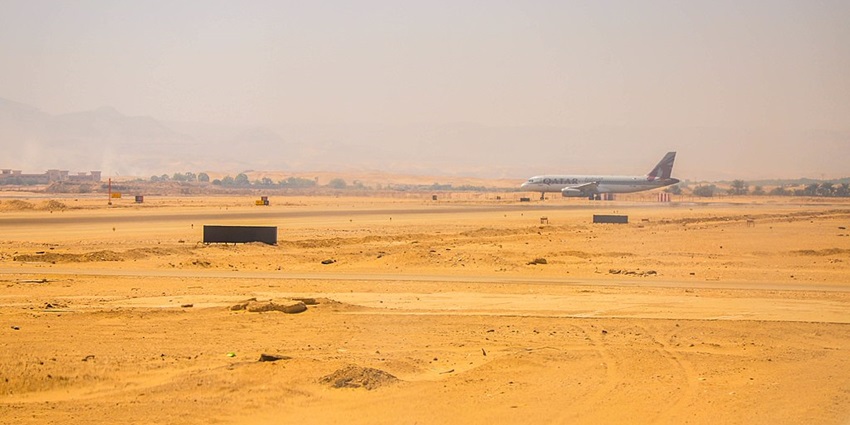 A long distance view of the Luxor airport runway showing a plane about to take off with sand around