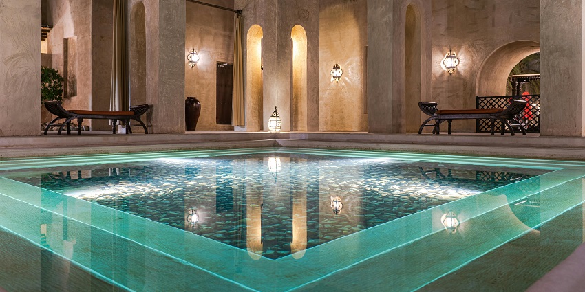 Open swimming pool inside a luxurious hotel reflecting light and two side benches