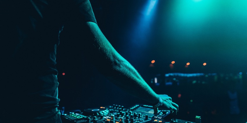 A person operating a DJ set in different blue tones with a blurred background of a club.