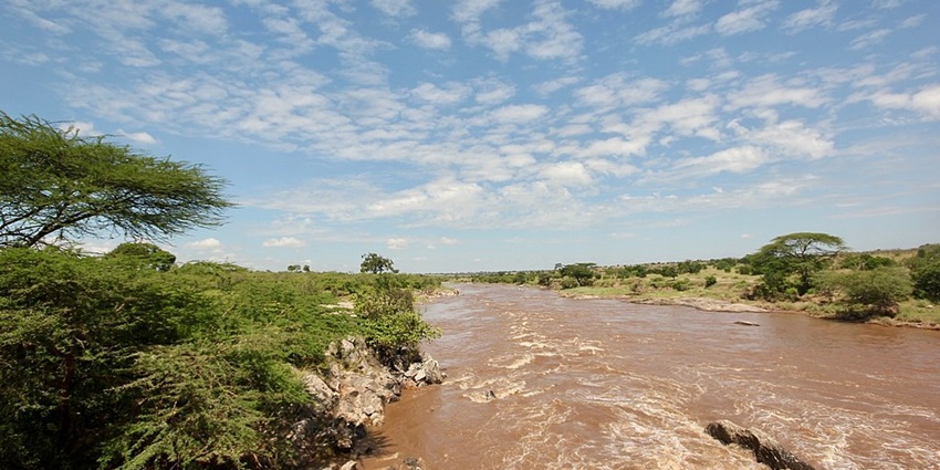 Mara River with brown sandy water and greenery on both sides of the river under a cloudy sky