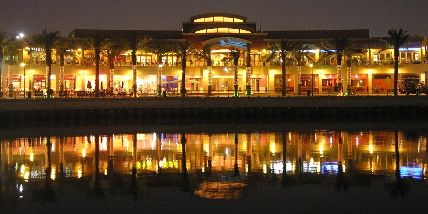 Scenic waterfront area with restaurants, shops, and a marina, showing Kuwait nightlife.
