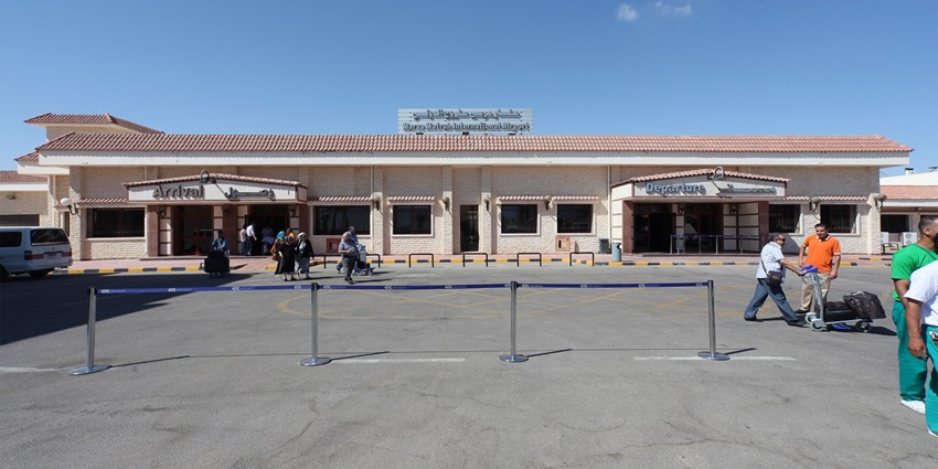 Front view of the Marsa Atruh airport showing a man pushing luggage trolley and other people