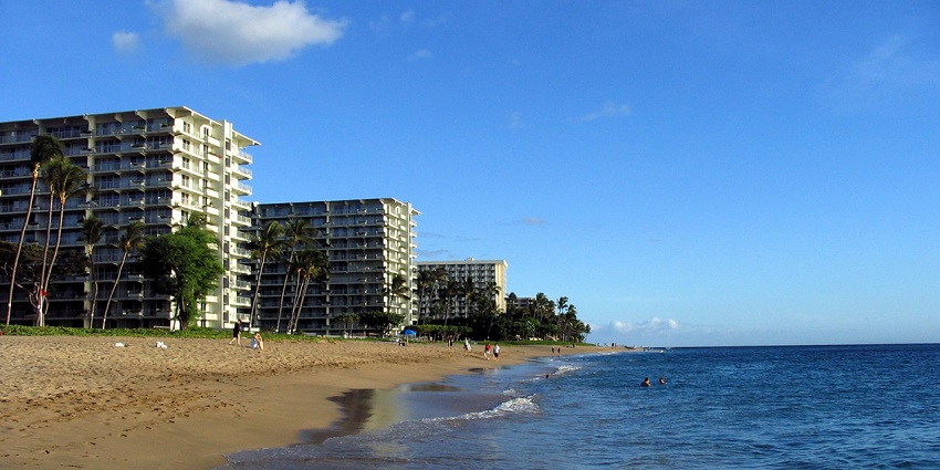 People are enjoying the sea at Kaanapali Beach, surrounded by lofty buildings and palm trees