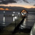 A well-lit pier on Mauritius Beach at night with lamps and a sunset in the background.