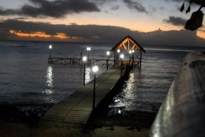 A well-lit pier on Mauritius Beach at night with lamps and a sunset in the background.