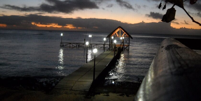 A well-lit pier on Mauritius Beach at night with lamps and a sunset in the background.