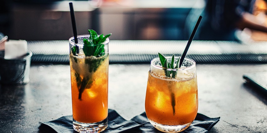 Two glasses of orange mojitos served with mint leaves and straws on black plates