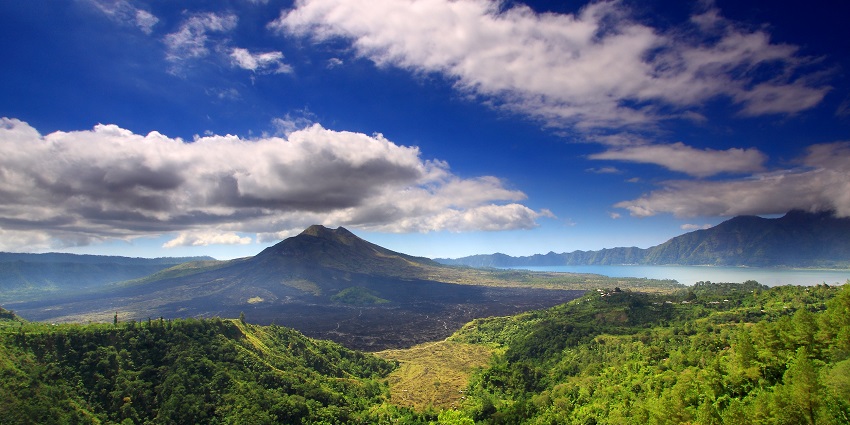 A view of volcanic Mount Batur with a lake on the right surrounded by lush greenery in Bali.