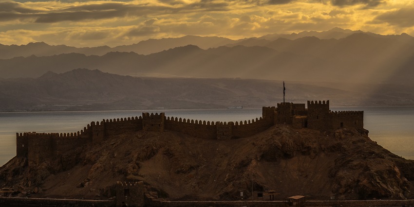 From the cloudy sky, the rays of the sun are shining through and there is a monument
