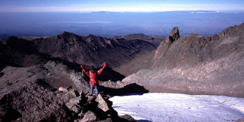 A hiker is celebrating on the top of a mountain peak in the Mount Kenya National Park