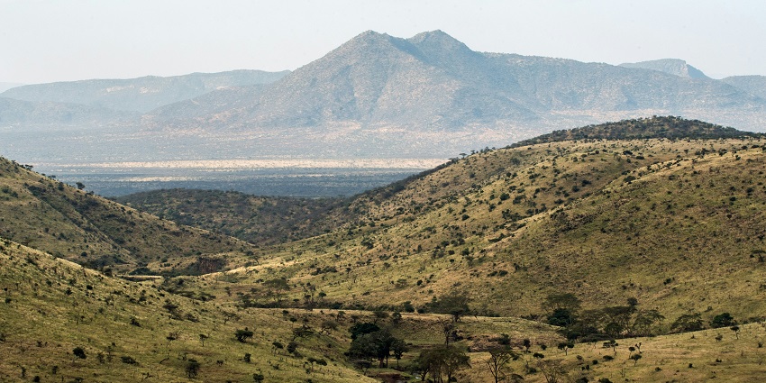 An empty road surrounded by greenery and hills of Mount Ololokwe visible straight ahead.