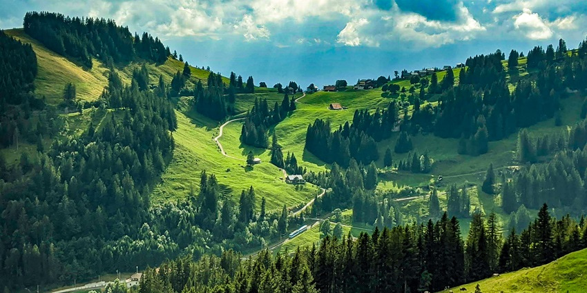 A picture of a scenic hill station in Switzerland with vast views of greenery and a blue sky