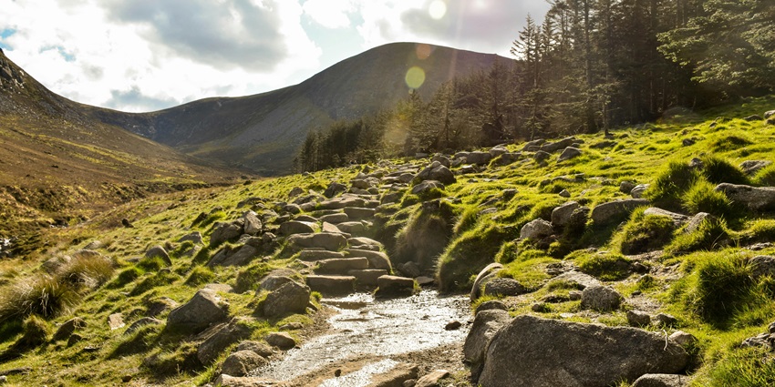 An image of a mountain landscape with a stone path, under a partly cloudy sky.