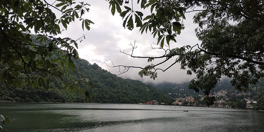 Scenic view of a serene Naini Lake with a backdrop of cloud-covered hills in the background in Nainital.