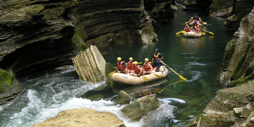 Three rafting boats are present in a valley that has people in it for river rafting