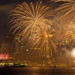 Fireworks burst in different colours above a cityscape during New Year celebrations.