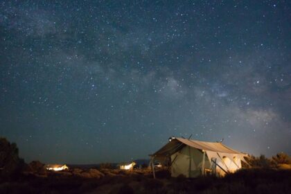 A vehicle loaded with bags and a person standing over the car observing the night sky