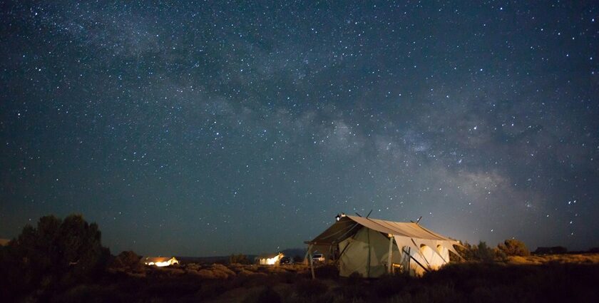 A vehicle loaded with bags and a person standing over the car observing the night sky