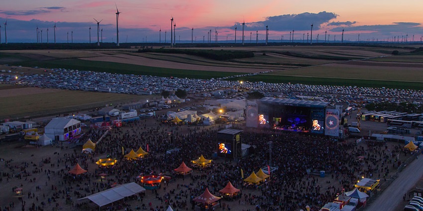 A crowd of people enjoying a rock concert at the Nova Rock Festival, with a large stage and colorful lights in the background.