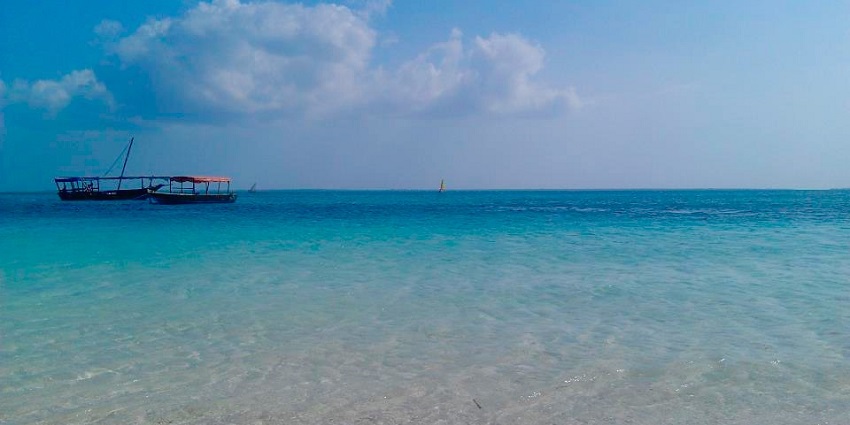 A clear water with different hues of blue has boats on it that surround the Nungwi beach.