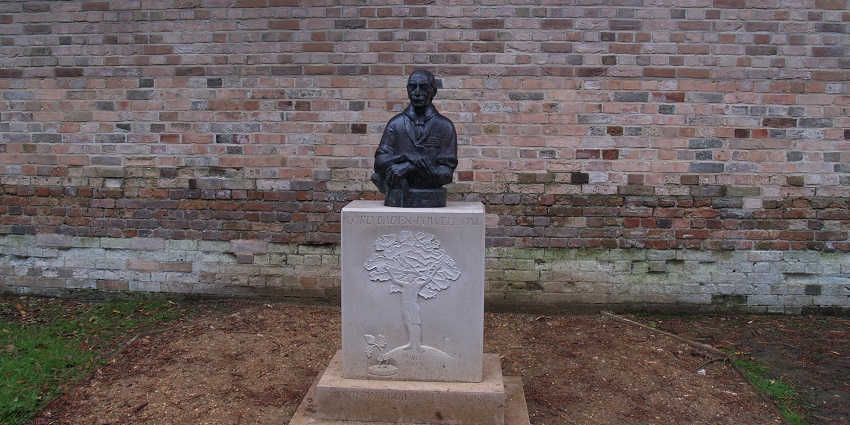 A carved statue of Lord Baden Powell presented in a Baden Powell Memorial outside.