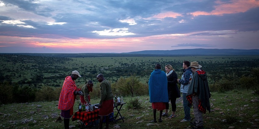 People camping and drinking at the Ol Kinyei Conservancy and mountains in the background.