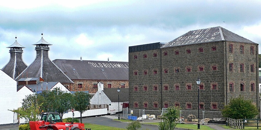 An image of the historic stone building of Old Bushmills Distillery, with its name painted on the roof.