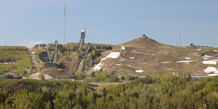 An aerial view of Canada Olympic Park in Calgary with ski jumps and snow-covered slopes.