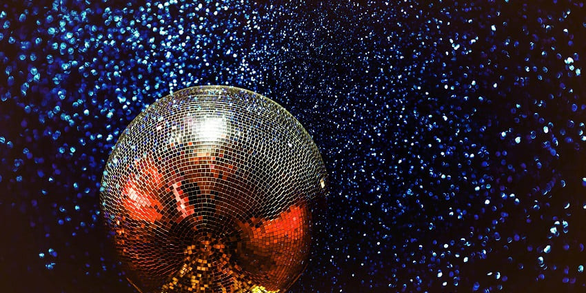 A huge silver disco ball reflecting vibrant colours and hanging from a glittery blue roof.