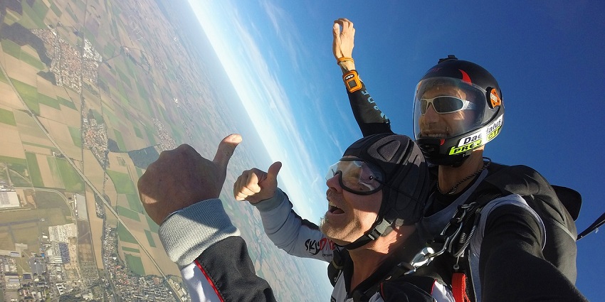 A view of skydiving with a vibrant sunset, yellow sky, and a parachute in the air.