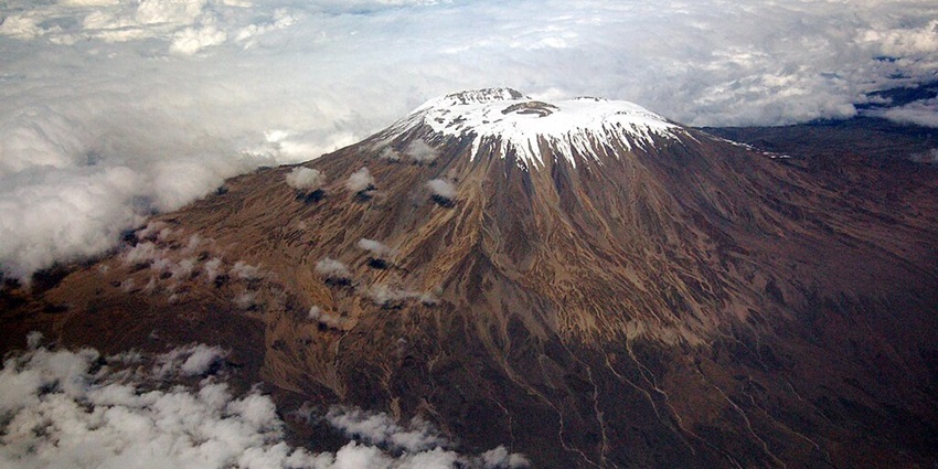 Peak of Mount Kilimanjaro covered in snow and the mountain half covered in clouds