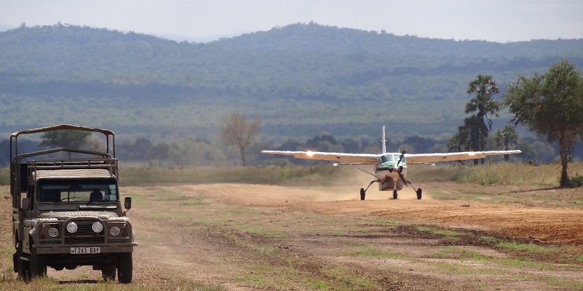 An airplane landing and dust in the air, a rover parked at a distance from Mikumi National Park.