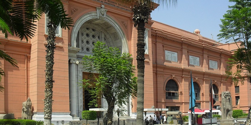 An outside view of a museum with orange outer coloring that has greenery surrounding it