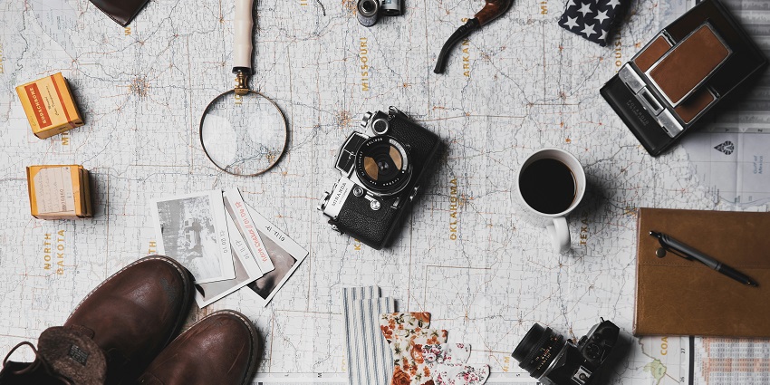 An image of travel things - a camera, a pair of shoes, a dairy and many more.