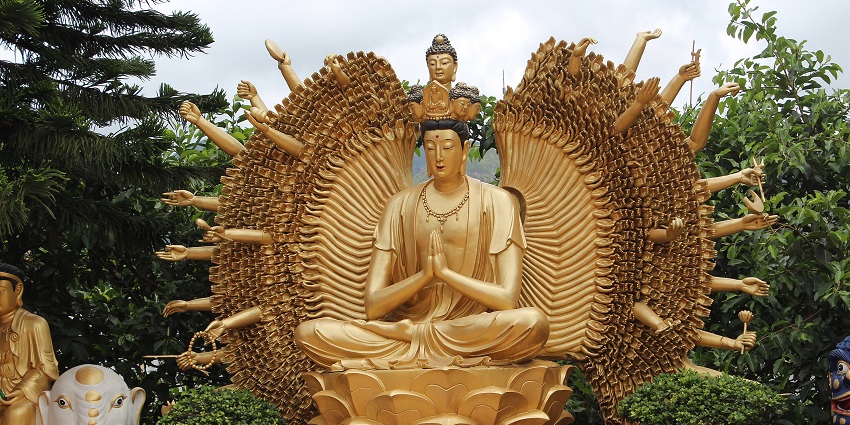 Image of Golden Buddha statue amidst lush greenery and under clear blue sky in Hong Kong