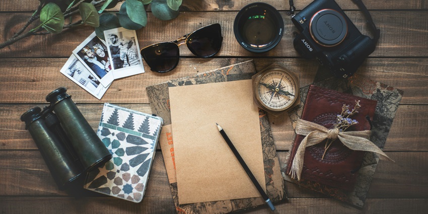 An image of travel things - a camera, pair of binoculars, a dairy, compass and more.