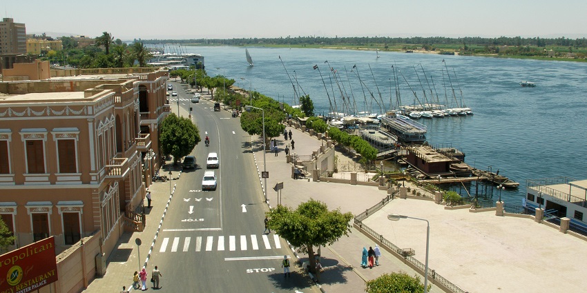 Busy road in Luxor with moving cars, motorcycles and people walking on the sidewalks