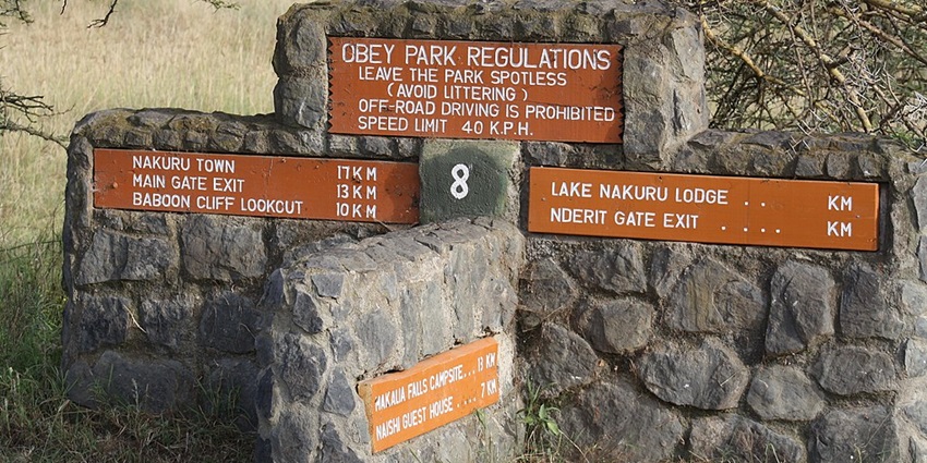 Multiple signage set in the rocks with Lake Nakuru National Park rules and distances