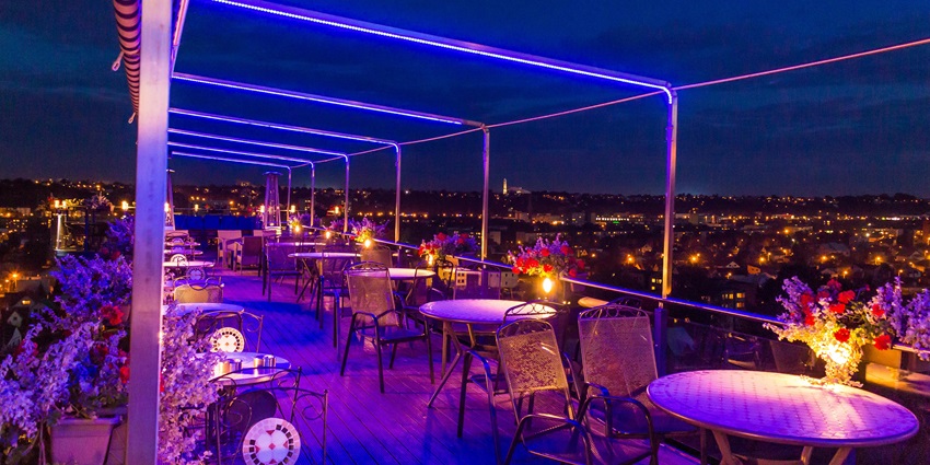 Rooftop restaurant with vibrant blue and pink lighting and flower lamps on each table