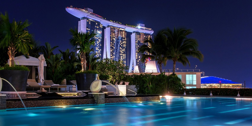 Swimming pool club with beach chairs, palm trees and highrise building in the background