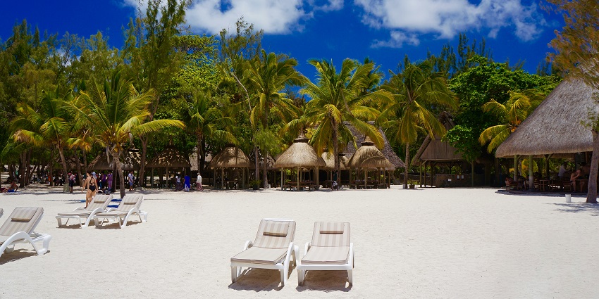 A beach is featuring two armchairs in the middle, with trees and hut-like shelters behind.